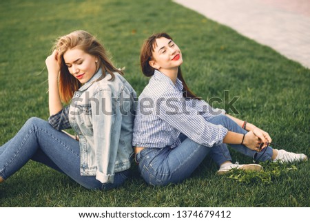 two beautiful young and stylish girl sitting in a summer city on a grass