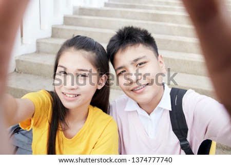 Couple Young asian teenager boy and girl sitting on stair and taking their photo selfie by smartphone