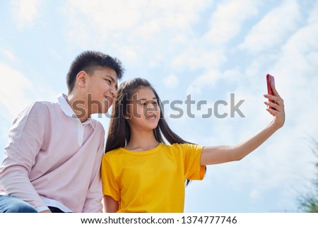 Portrait of a smiling young asian couple sitting on the railing taking a selfie outdoor
