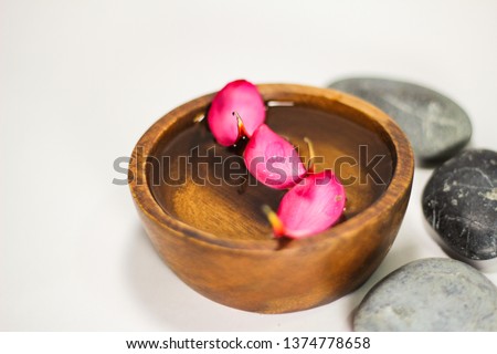 Spa and zen concept. Three frangipani flower petals floating in wooden bowl with three zen stones laying against white background. 