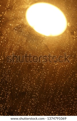 There are many rain drops on the window at night with a lamp reflection.