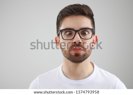 funny man with ugly face and crooked eyes wearing glasses - young man casually dressed in white with gray background   Royalty-Free Stock Photo #1374793958