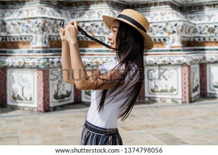 Side view Portrait of beautiful Thai woman in white T-shirt with brown panama taking photo with mirrorless camera at Buddhist Temple.