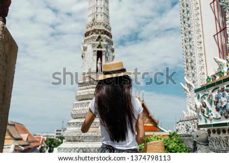 Back View Of Young Attractive female Asian traveler with hat standing in historical temple at bangkok.wearing brown boater.windy and summer day.