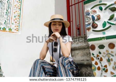 Attractive Asian tourist backpacker sitting resting on stone stairs  while sightseeing the temples Bangkok,Thailand.