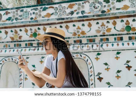 Portrait of relaxed attractive Asian traveler using smartphone at Buddhist Temple.