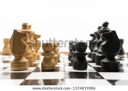 two sides of black and white chess pieces, which are made of wood, are facing each other. There is a white background for placing posts