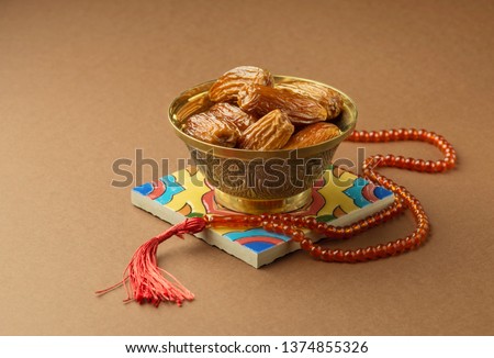 A metallic antique bowl filled with sweet arabic date fruits, placed along with Islamic prayer beads. Ramadan Kareem photo. Royalty-Free Stock Photo #1374855326