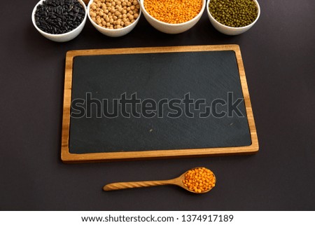 Overhead photo of various legumes in bowls with spices, with copy space, on black background.Pulse: lentils, mung bean, beans, chickpeas, black beans