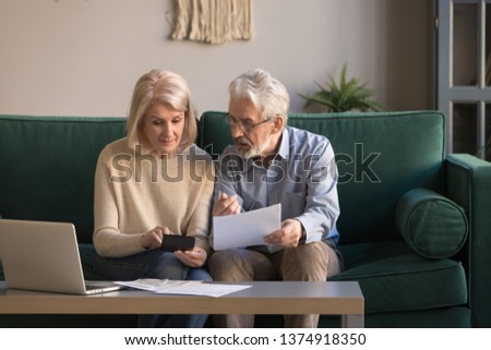 Serious mature couple calculating bills to pay, checking domestic finances, middle aged family managing, planning budget, expenses, grey haired man and woman reading bank loan documents at home Royalty-Free Stock Photo #1374918350