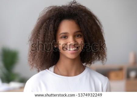 Head shot portrait of smiling African American teenage girl, feeling happy, posing for photo at home, beautiful positive mixed race teenager looking at camera, laughing, having fun