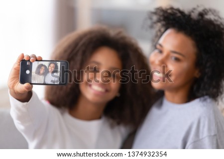 African American mother and teenage daughter taking selfie, smiling teen girl holding phone, happy mum posing for photo with child, close up mobile device, family having fun together with gadget