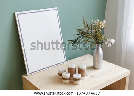 Vase with a plant and candles on a table near a picture with copy space. Place for text. Cozy interior concept