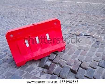 Red plastic barrier on the road from paving stones. Part of the road surface is damaged. It is blocked to avoid car accidents and damage to cars.