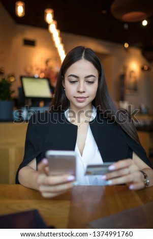 Gorgeous woman dressed in fashionable clothes online ordering via cellphone using credit debit card while relaxing in coffee shop during leisure in vacation. Female booking via mobile phone