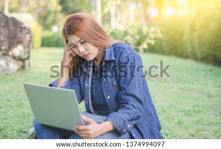 Asian women wearing denim shirts are sitting to think of creating new jobs in front of modern laptops. On the lawn area in the garden with warm orange light in summer
