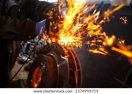 Close-up of a man sawing   bearing metal brake disk with a hand circular saw, bright flashes flying in different directions, in the background tools for an auto repair shop. Work of auto mechanics.