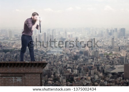 Handsome bearded man on a roof top taking picture of a city