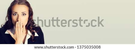 Portrait of surprised excited young business woman covering with hands her mouth, with empty copy space place for some text, advertising or slogan, over grey background. Business concept photo.