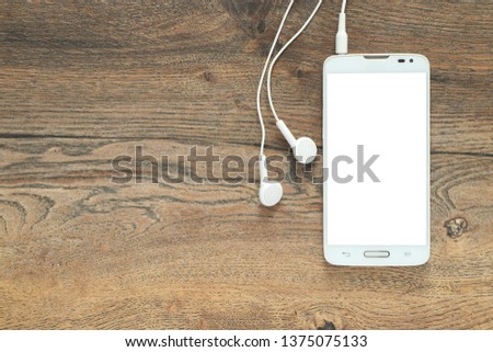 Smartphone with isolated white screen with connected earphones on the background of a wooden desk