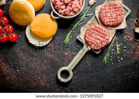 Raw burgers with ground beef, buns and tomatoes. On dark rustic background