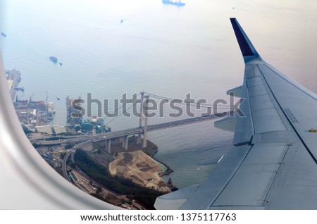 Plane flies over Hong Kong. Window seat on airplane overlooking to Kap Shui Mun bridge, between Tsing Yi and Ma Wan islands.