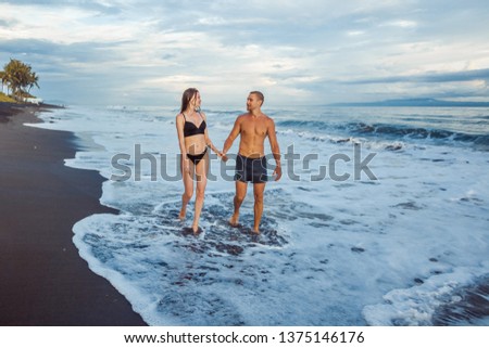 The girl and the man walk on the beach in swimsuits.