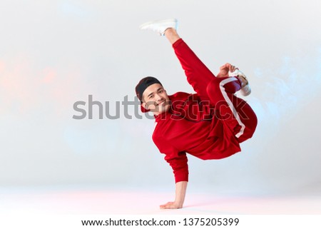 Stylish dressed in red sweatpants asian b-boy is performing kick in air, standing on hands while dancing break dance on white background. Freestyler doing air baby freeze Royalty-Free Stock Photo #1375205399