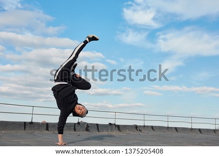 Young Korean urban style male dancer working out, performing breakdance moves, handstand on the top roof outdoor against blue sky. Royalty-Free Stock Photo #1375205408
