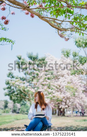 spring season with full bloom pink flower travel concept from beauty asian woman enjoy sit under the big tree with see cherry blossom with soft focus flower background