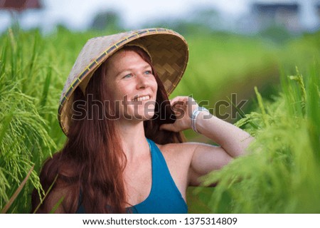 young happy and beautiful red hair woman in traditional Asian farmer hat smiling cheerful isolated on green rice field in Asia tourist trip and Summer holidays travel and adventure