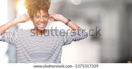 Beautiful young african american woman wearing glasses over isolated background Smiling pulling ears with fingers, funny gesture. Audition problem