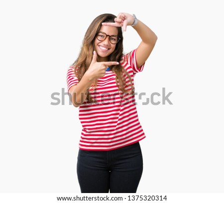 Young beautiful brunette woman wearing glasses and stripes t-shirt over isolated background smiling making frame with hands and fingers with happy face. Creativity and photography concept.