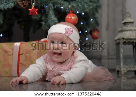 little girl five months in a pink dress lying on the floor by the Christmas tree with gifts