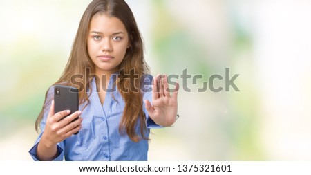 Young beautiful brunette business woman using smartphone over isolated background with open hand doing stop sign with serious and confident expression, defense gesture