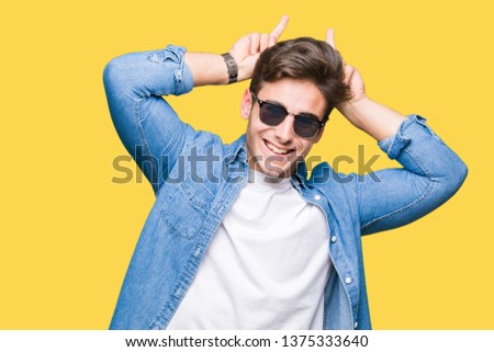 Young handsome man wearing sunglasses over isolated background Posing funny and crazy with fingers on head as bunny ears, smiling cheerful