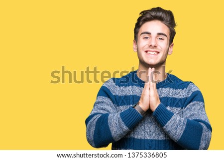 Young handsome man over isolated background praying with hands together asking for forgiveness smiling confident.