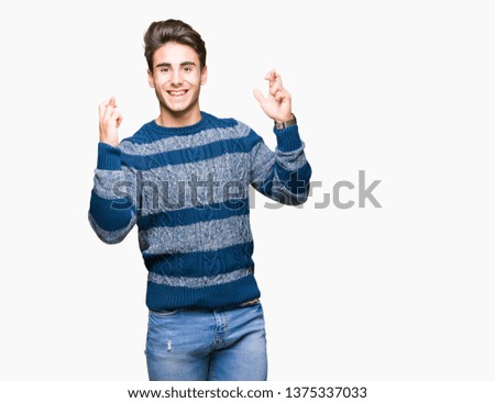 Young handsome man over isolated background smiling crossing fingers with hope and eyes closed. Luck and superstitious concept.