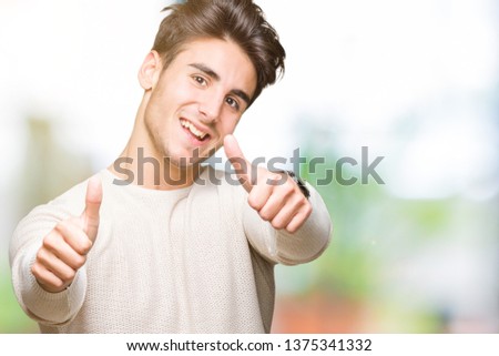 Young handsome man over isolated background approving doing positive gesture with hand, thumbs up smiling and happy for success. Looking at the camera, winner gesture.