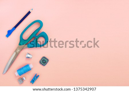 Accessories and tools for sewing scissors, pencil, thimble, thread reel, clothespin, foot for sewing machine, plain blue on a pink background. Top view, flat lay. Copy space for text.