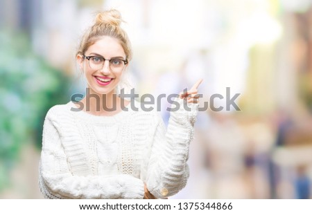 Young beautiful blonde woman wearing glasses over isolated background with a big smile on face, pointing with hand and finger to the side looking at the camera.