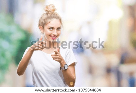 Young beautiful blonde woman wearing white t-shirt over isolated background pointing fingers to camera with happy and funny face. Good energy and vibes.
