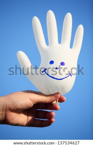 hand holding smiling glove against blue sky.