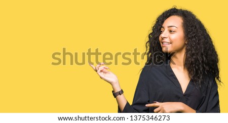 Young beautiful girl with curly hair wearing elegant dress with a big smile on face, pointing with hand and finger to the side looking at the camera.