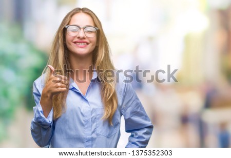 Young beautiful blonde business woman wearing glasses over isolated background doing happy thumbs up gesture with hand. Approving expression looking at the camera with showing success.