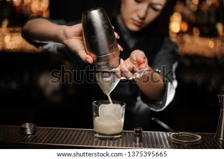 Close shot of female bartender pouring cocktail adding sour mix from shaker in glass with ice
