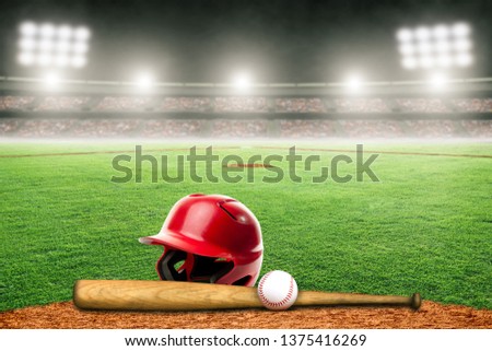 Baseball helmet, bat and ball on field at brightly lit outdoor stadium. Focus on foreground and shallow depth of field on background and copy space.