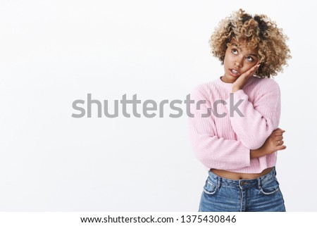 Girl feeling boring looking at clock with bored expression pissed time moving slowly leaning head on hand gazing at upper left corner uninterested. drained standing spaced out gloomy over white wall