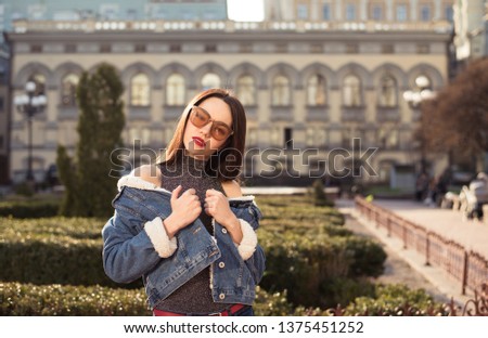 Portrait of young happy cheerful beautiful woman with dark hair dressed in jeans jacket in nice sunny day in city park