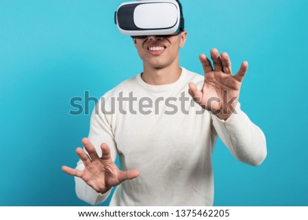 Close up of young man wearing  virtual reality headset on blue background in studio and gesticulating with hands. Front view - Image